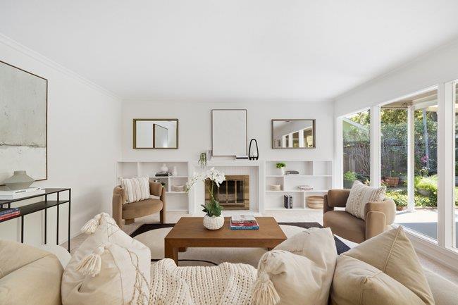 Staged living room with a fireplace, neutral seating, and glass doors overlooking a garden.