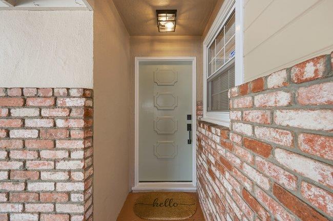 Covered home entrance with brick walls, a pale paneled door, and a hello doormat.