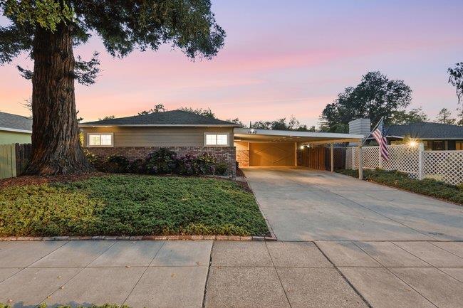 Single-story home's front exterior at dusk, with a wide driveway and large mature tree.