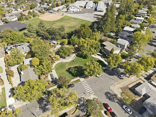 Aerial view of a tree-lined neighborhood green space beside homes and streets.
