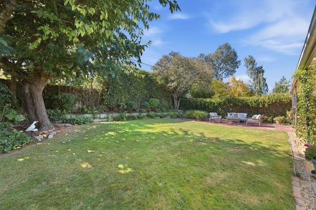 Backyard lawn with mature trees, landscaped borders, and a brick patio seating area.