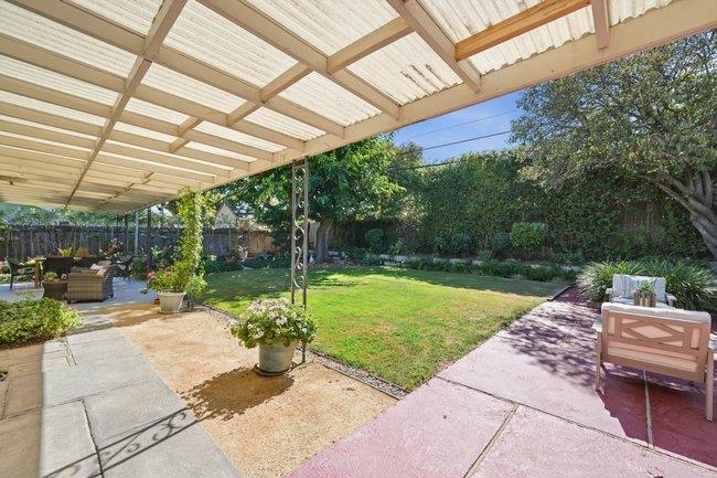 Backyard lawn bordered by stone patios, with a covered pergola and outdoor seating.