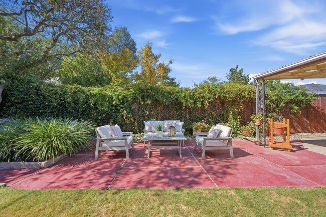 Red paved patio with cushioned lounge chairs and a coffee table beside a lawn and tall hedges.