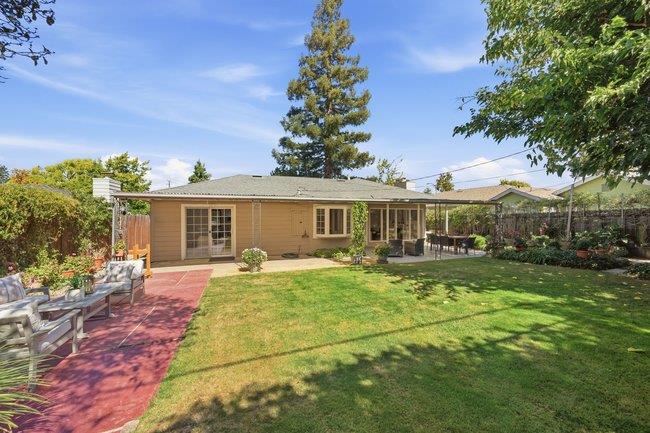 Single-story home's backyard with a broad lawn, red patio, and covered outdoor dining area.