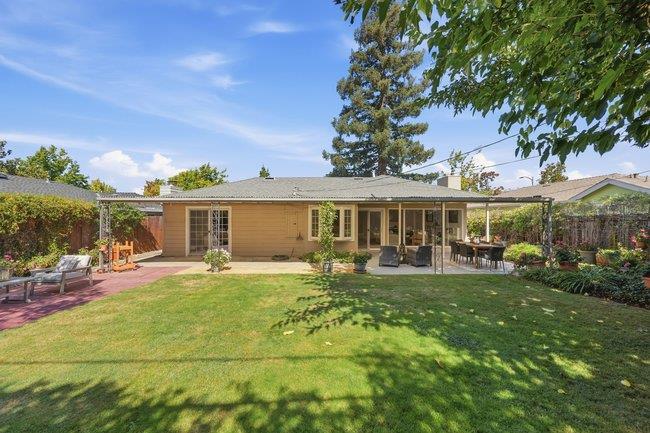 Home’s rear exterior with a covered, furnished patio and a broad lawn.