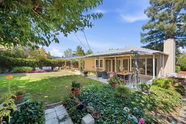 Single-story home with a covered patio and outdoor dining area overlooking a leafy garden.