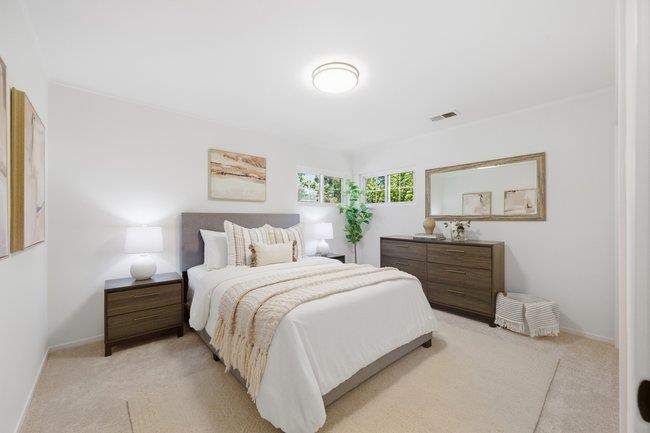 Staged bedroom with a white bed, dark wood furniture, and small windows above the headboard.