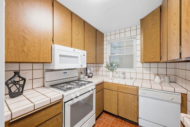 Kitchen with honey-toned cabinets, tiled counters, and a white gas range beneath a microwave.