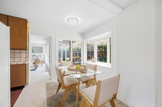 Bright dining area with a glass-top table, wooden chairs, and large garden-facing windows.