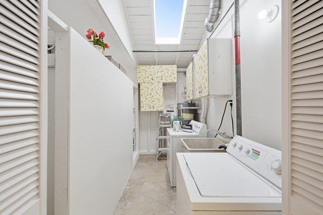 Laundry room with a white washer and utility sink beneath a skylight.