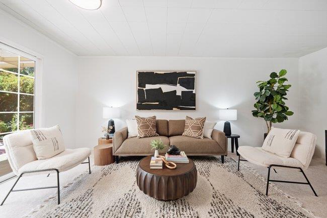 Living room with a brown sofa, cream chairs, round coffee table, and tall potted plant.