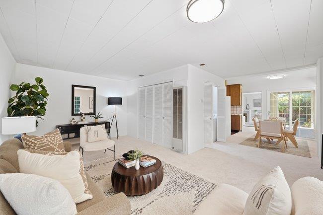 Staged living room with cream seating, a dark round coffee table, and a dining area by glass doors.