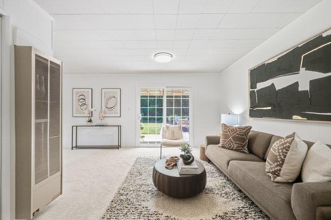 Living room with a gray sofa, round coffee table, textured rug, and sliding glass doors to a garden.