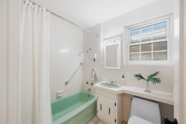 Bathroom with a mint-green bathtub, white vanity, and window above the counter.