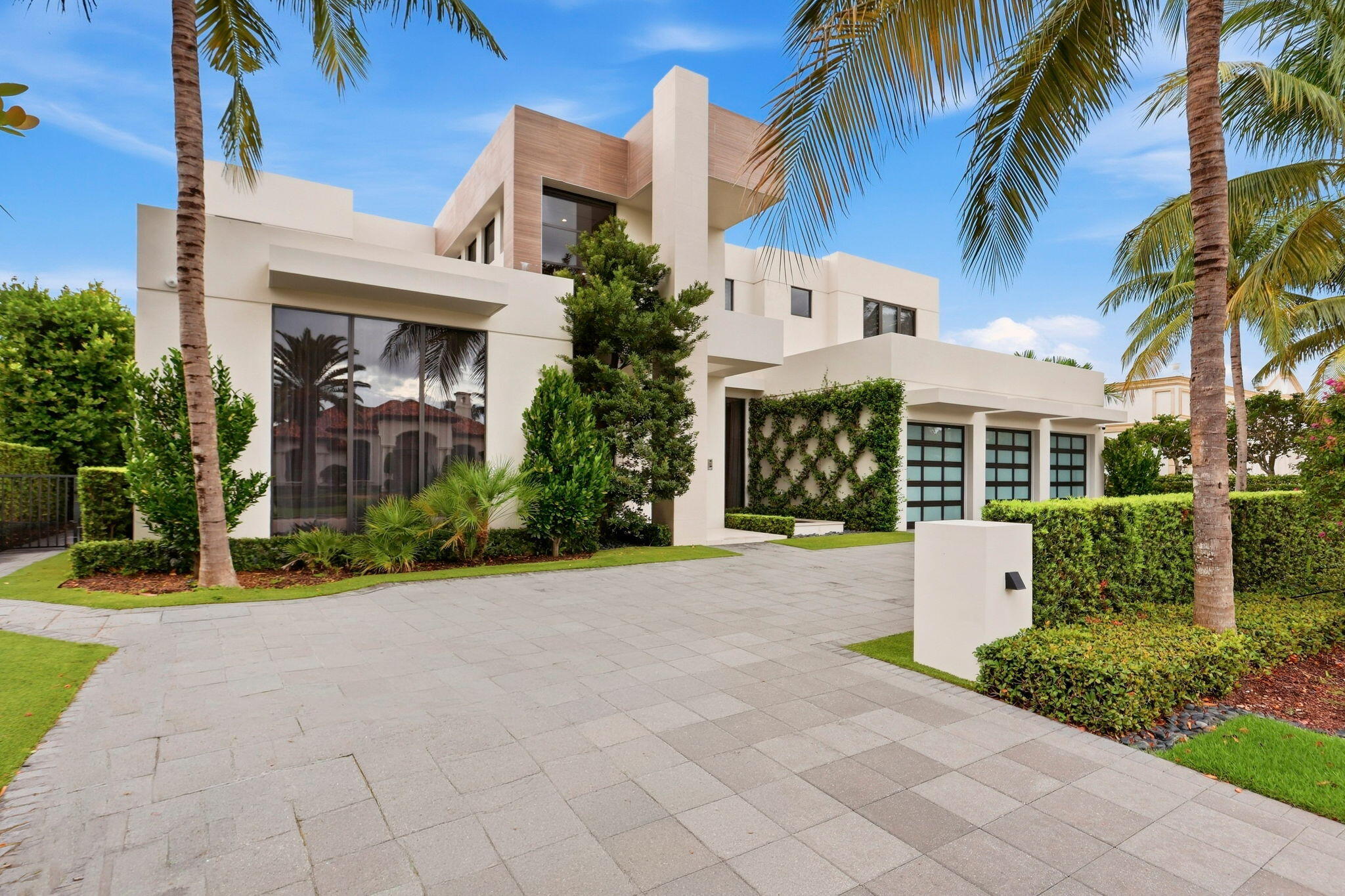 Modern white home with palm trees, landscaped grounds, and a wide paved driveway.