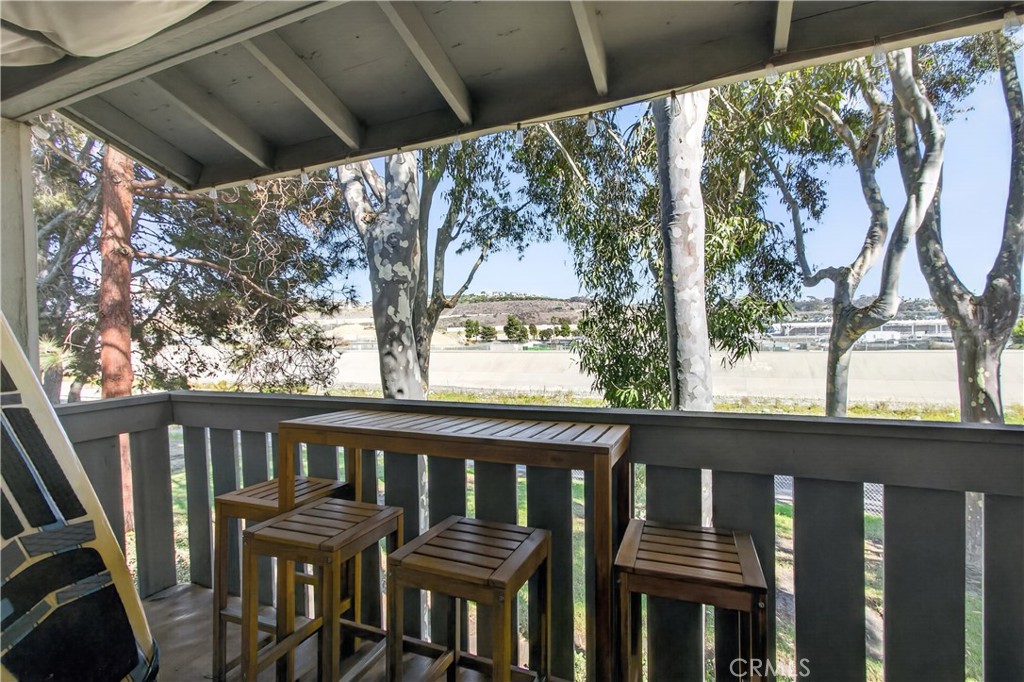 Covered balcony with a wooden bar-height table and stools overlooking trees.
