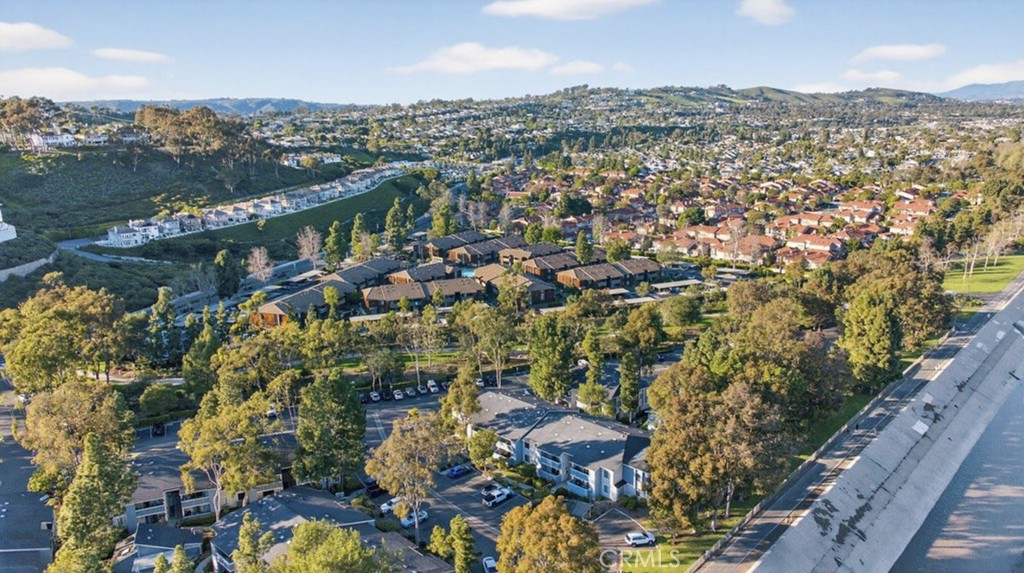 Aerial view of homes and low-rise buildings among trees, parking areas, and rolling hills.