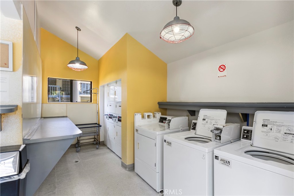 Communal laundry room with white washers and dryers, gray folding counters, and yellow walls.