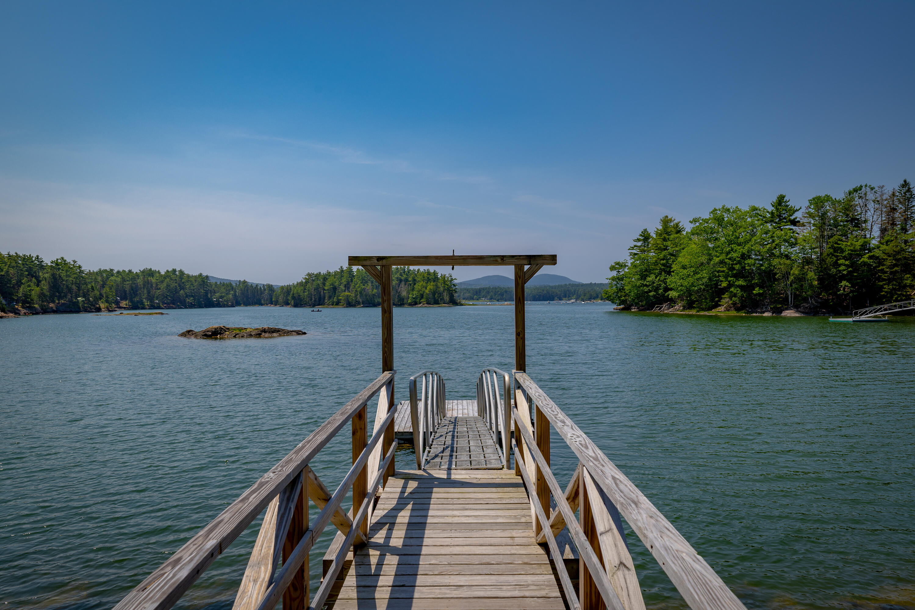 Wooden dock and swim ladder extending into a tree-lined bay with distant mountains.
