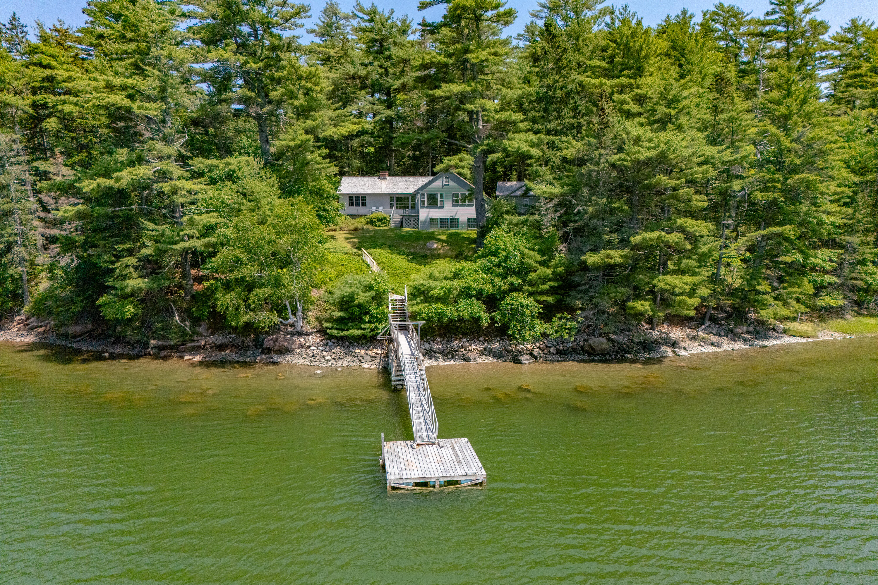 Waterfront home among pine trees, with a long dock and platform extending into the water.