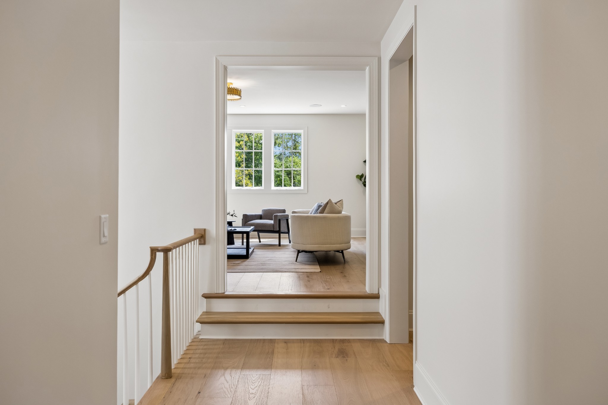Upstairs hallway with wood floors and railing opening onto a bright, furnished living room.