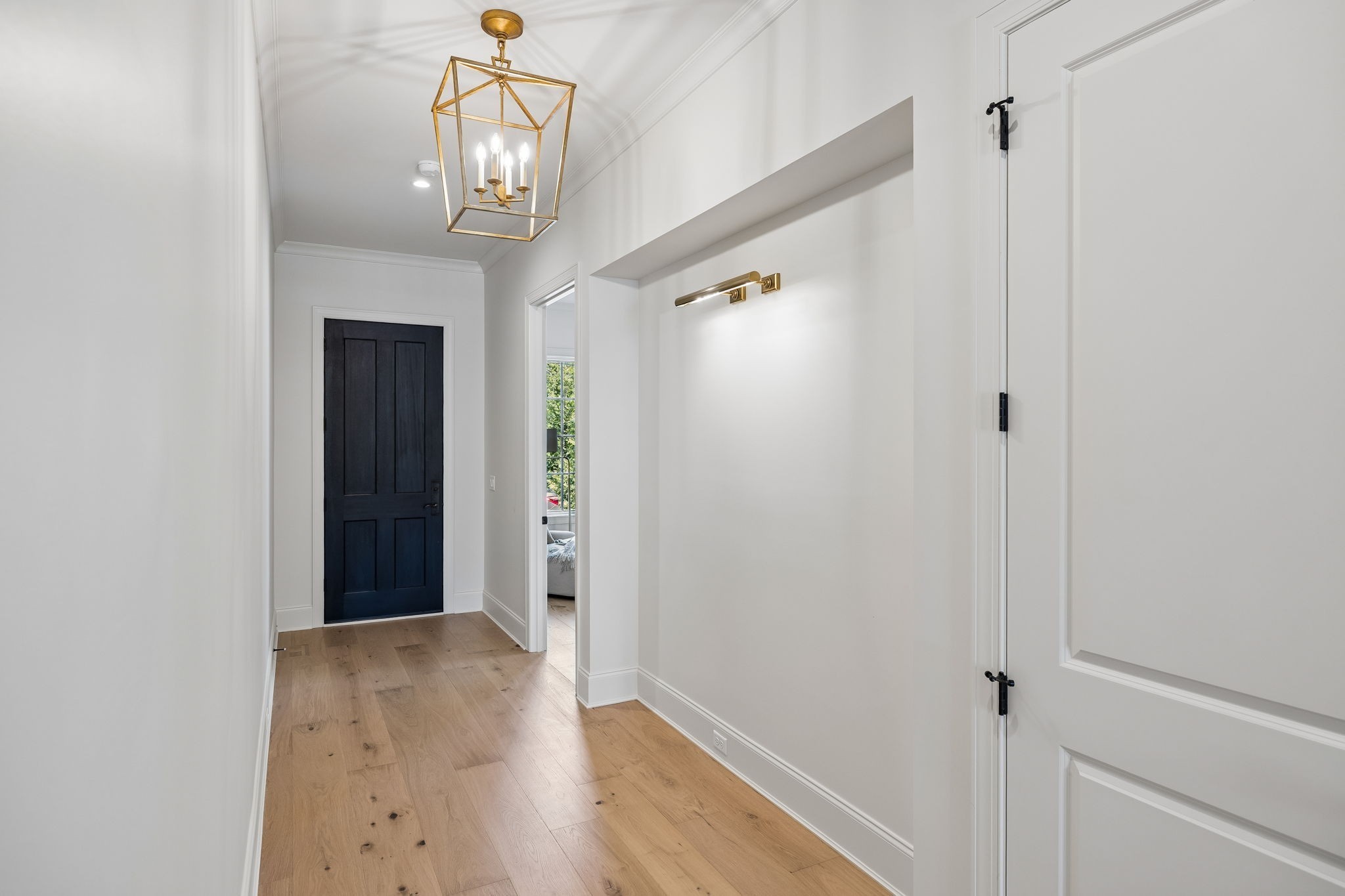 Entry hall with light wood floors, a black paneled door, and a brass geometric pendant chandelier.