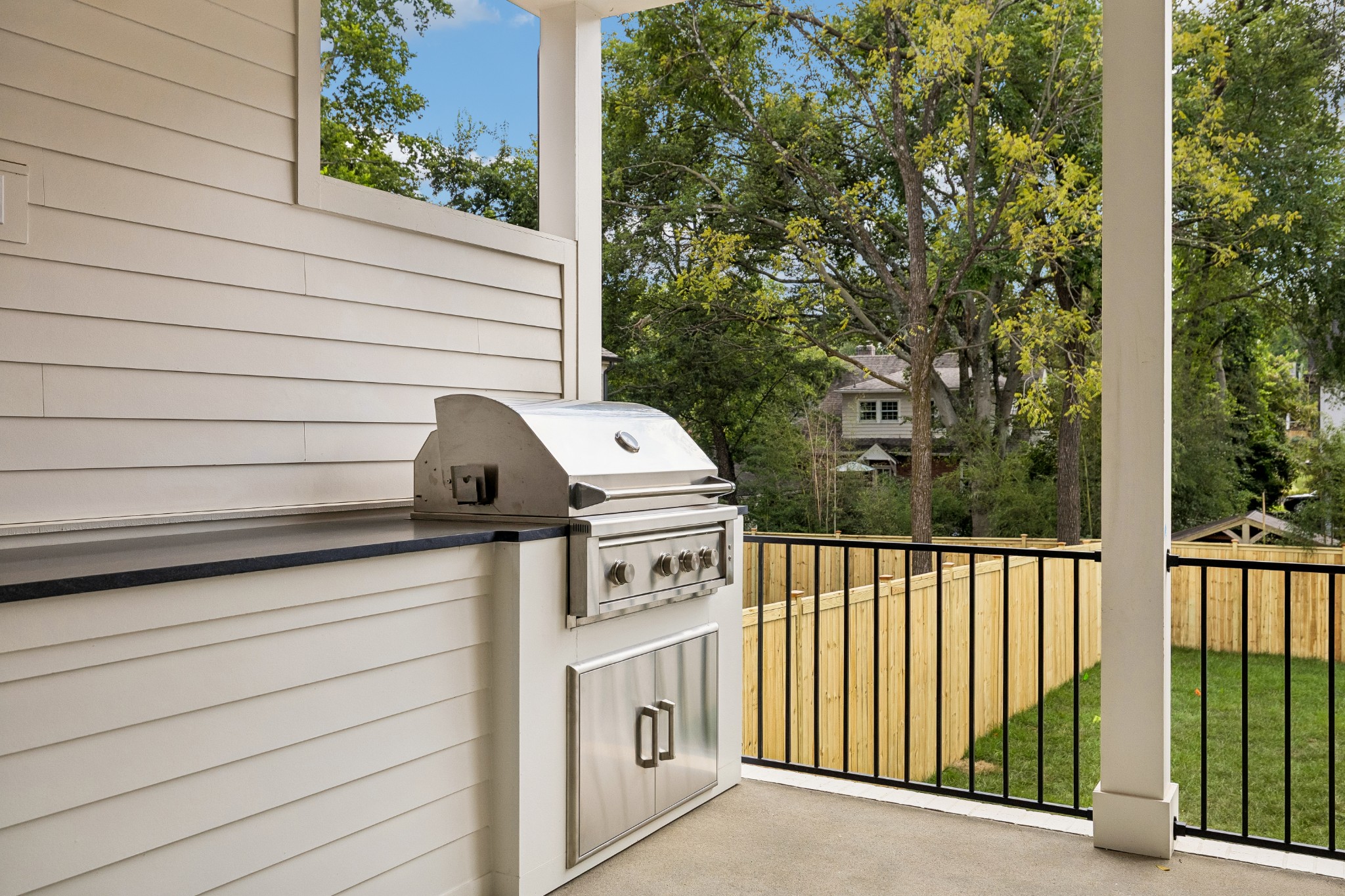 Covered patio with built-in stainless steel grill overlooking a fenced yard and mature trees.