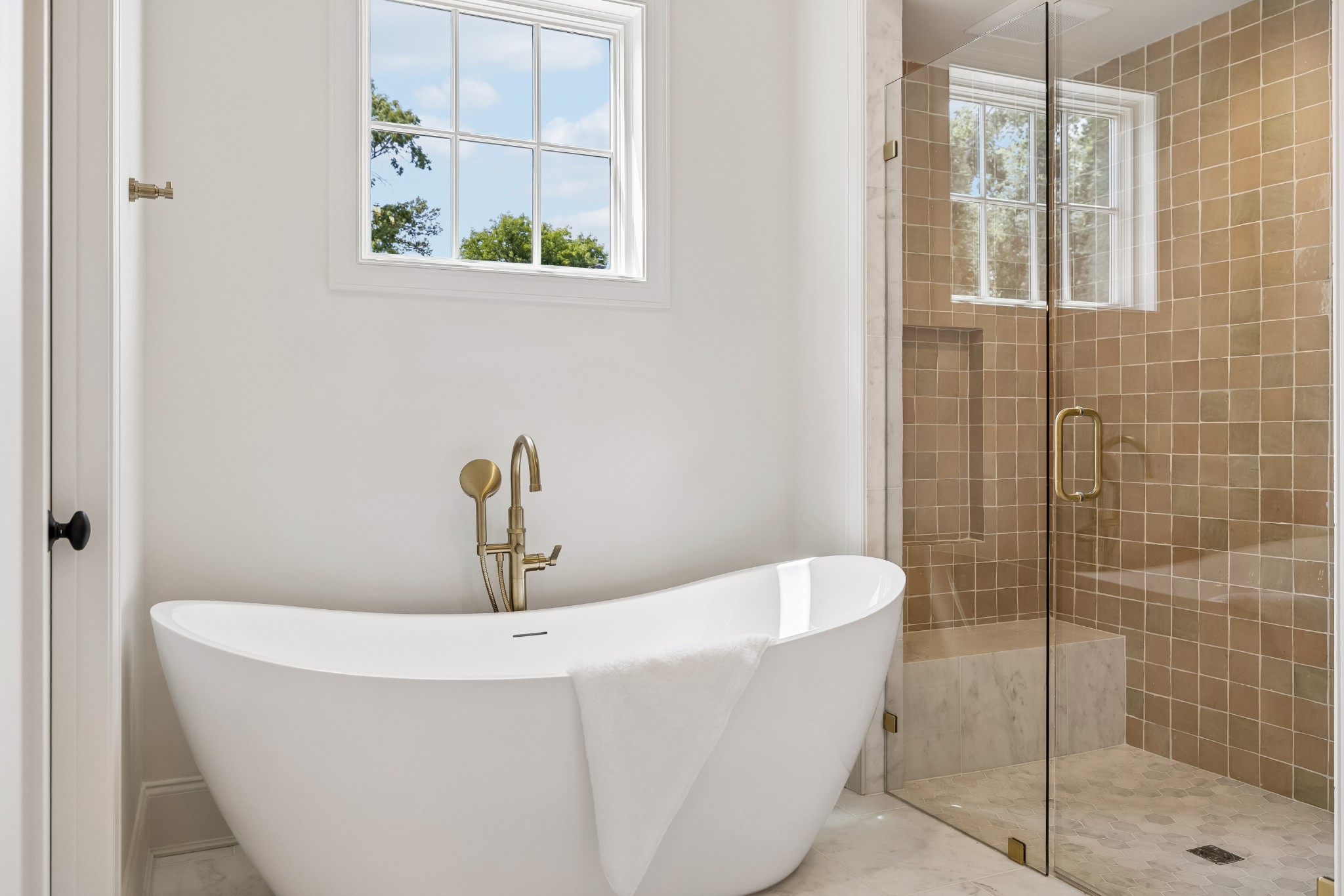 Bathroom with a freestanding tub, brass fixtures, and tan-tiled glass shower.