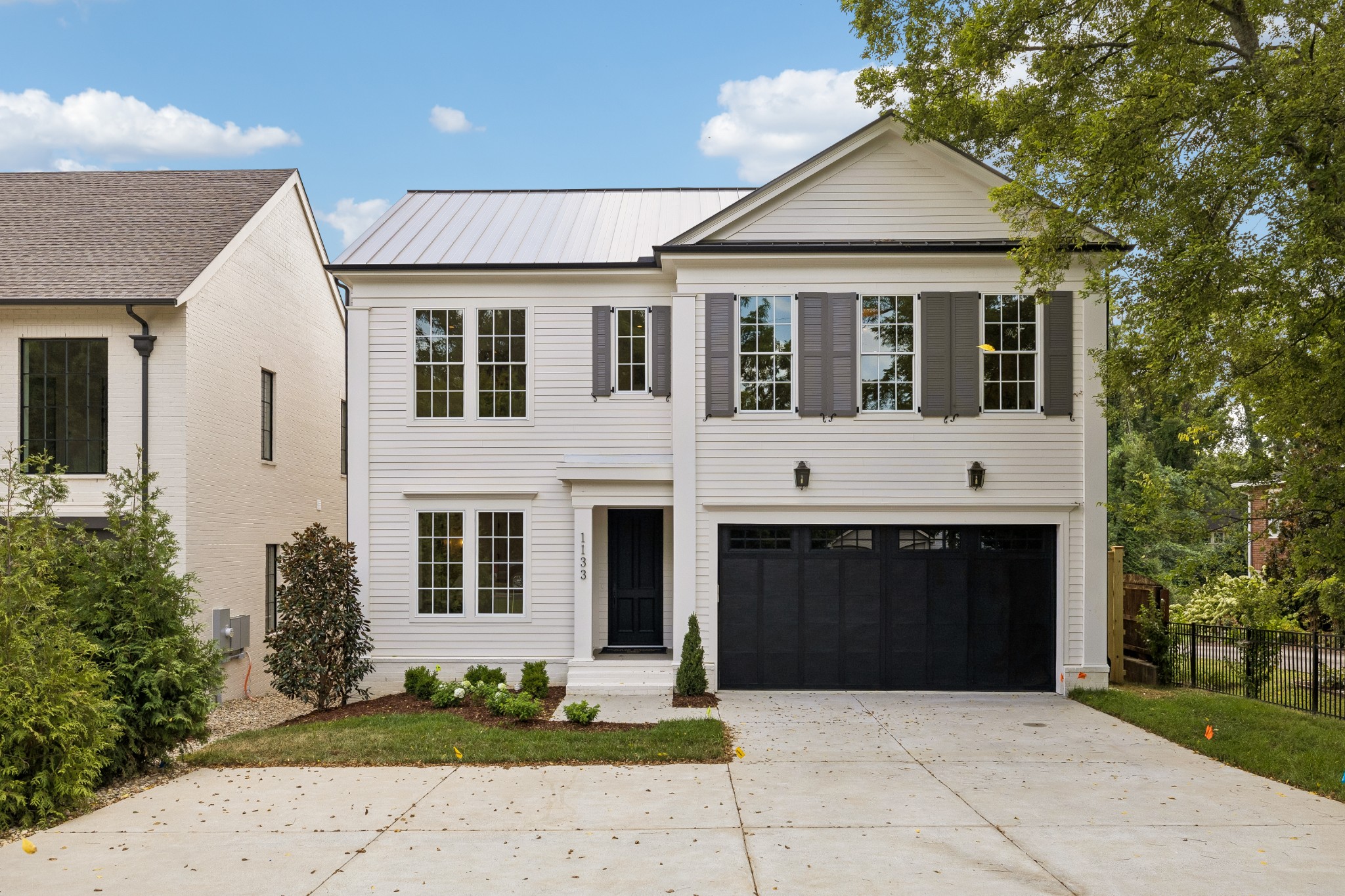 White two-story house with gray shutters, black double garage, and wide concrete driveway.