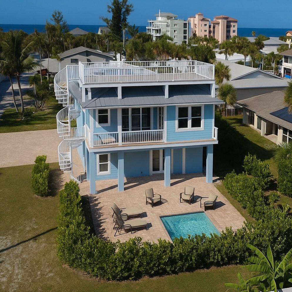Blue coastal home with rooftop deck and backyard pool, with the ocean beyond.