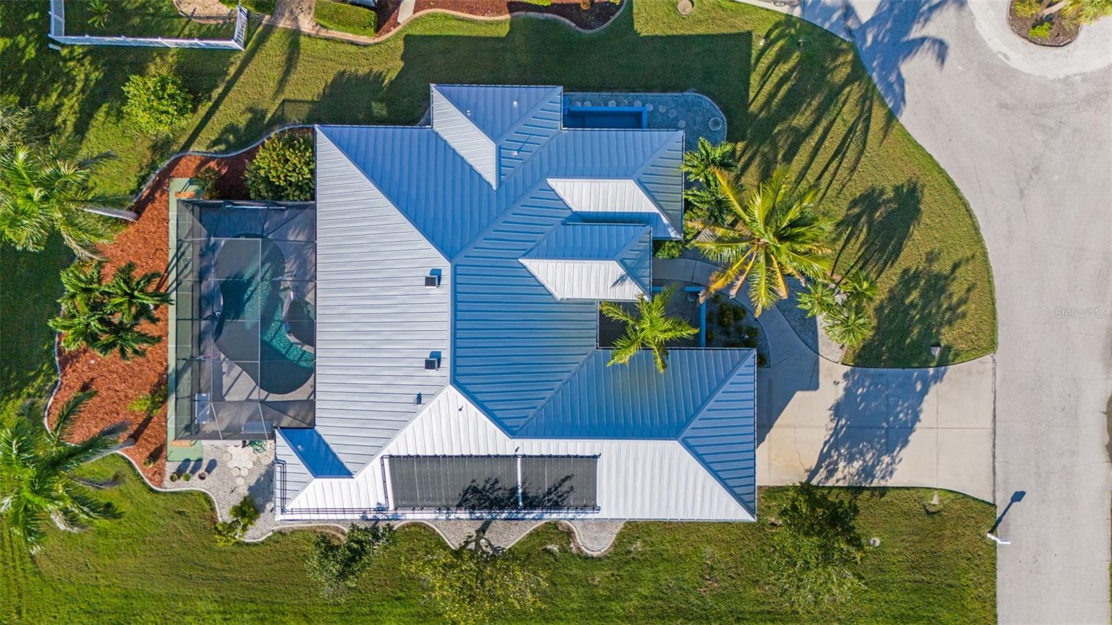 Aerial view of a house with a screened pool, light metal roof, and palm trees.