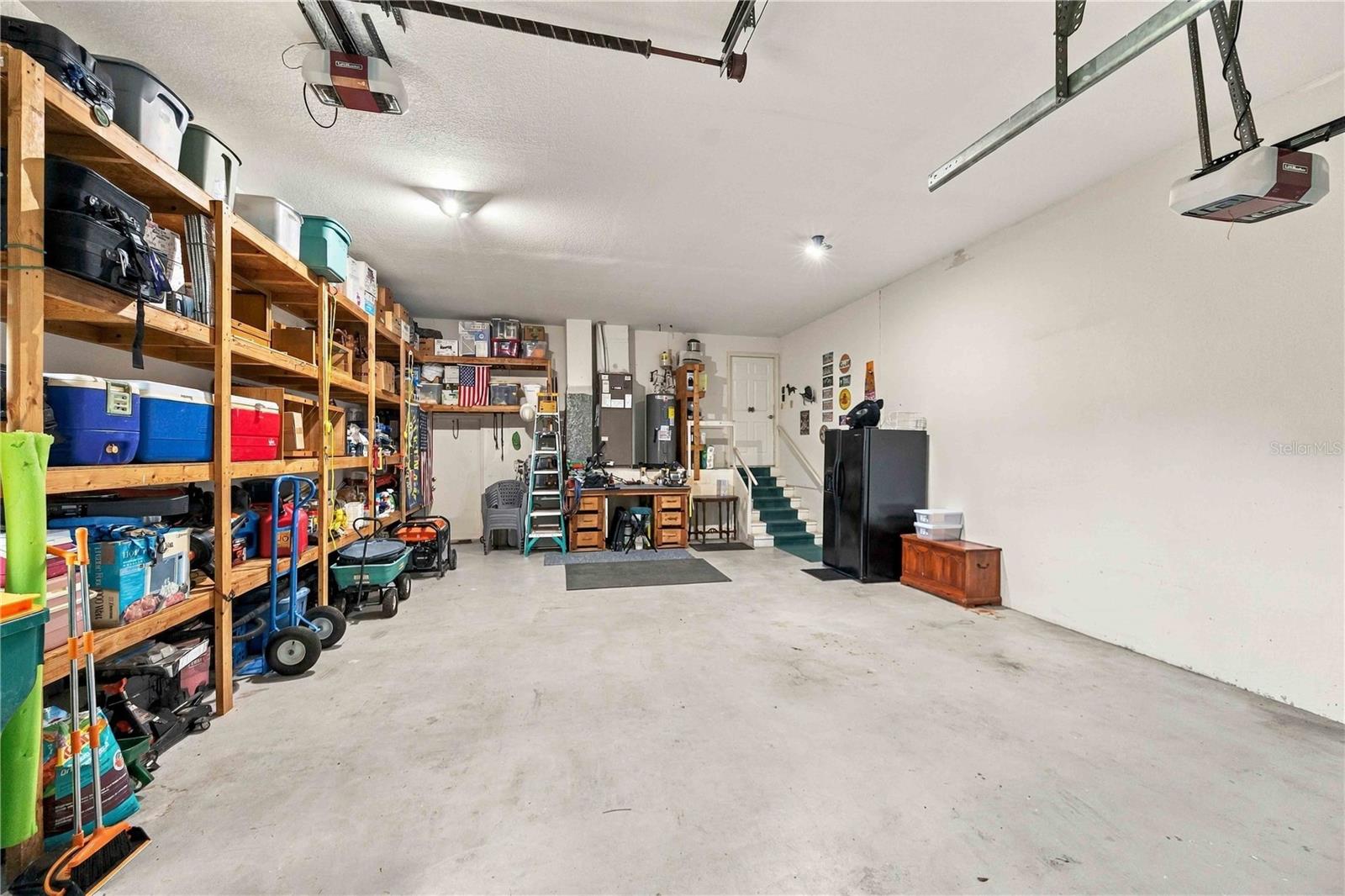 Spacious garage with extensive wooden storage shelves, a workbench, and stairs at the back.
