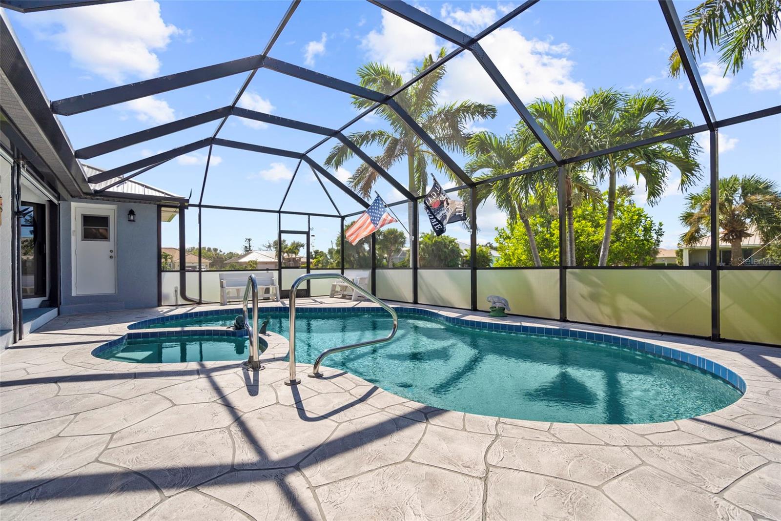 Curved swimming pool beneath a screened lanai, with a stamped-concrete deck and palm trees.