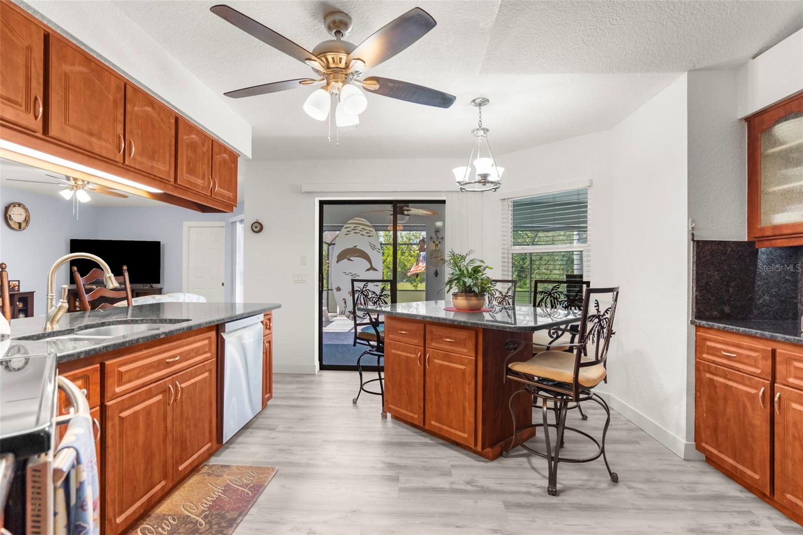 Kitchen with warm wood cabinets, a central island and dining stools beside sliding patio doors.