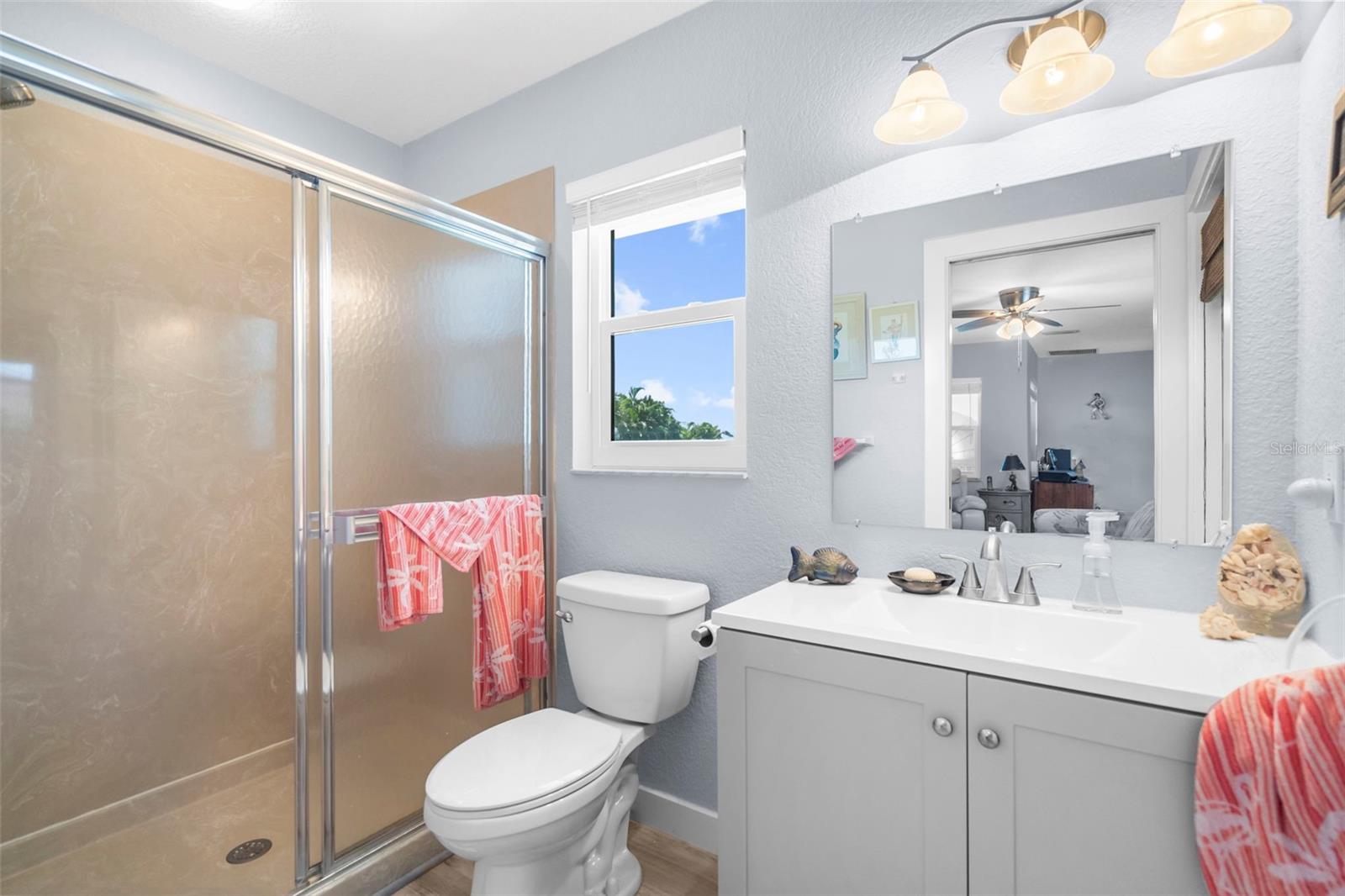 Bathroom with a glass-enclosed shower, white toilet, and gray vanity beneath a wide mirror.