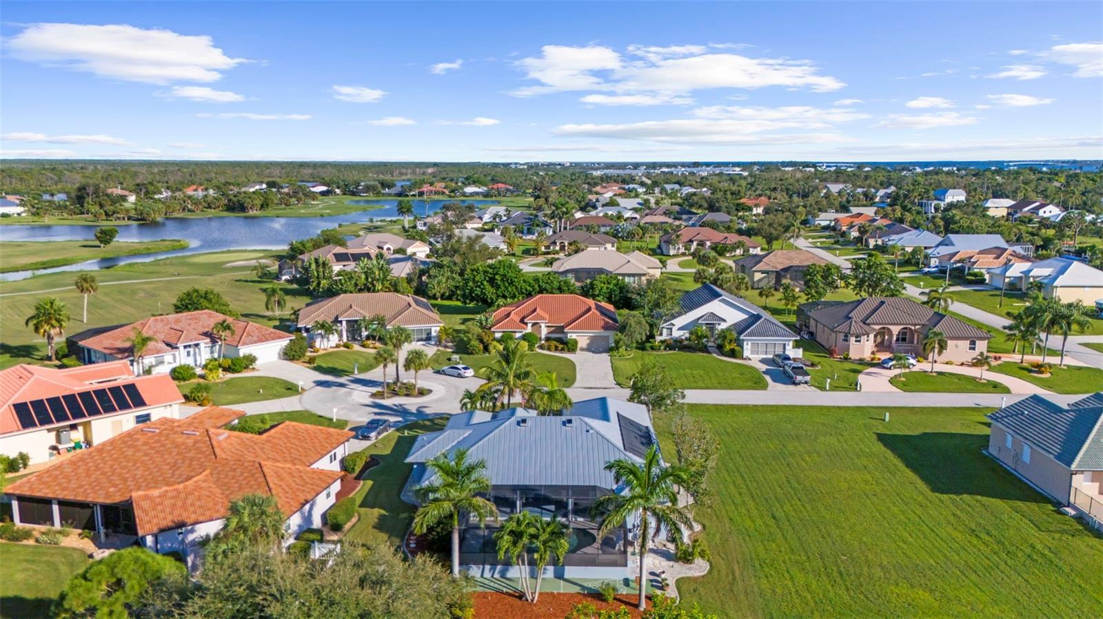 Aerial view of homes beside a winding lake, with a distant shoreline and blue sky.