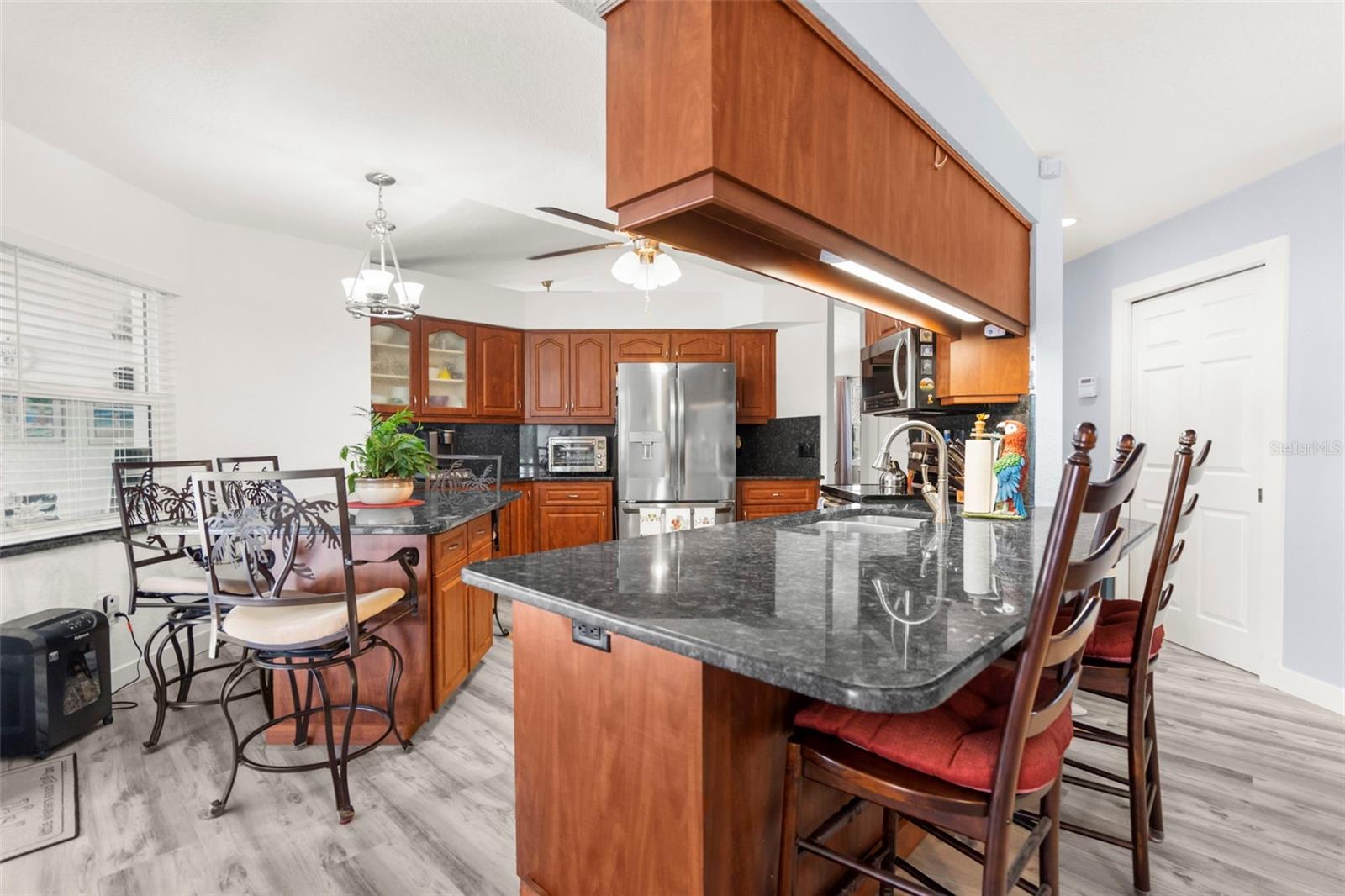 Kitchen with cherry wood cabinets, granite island and bar stools, stainless steel appliances, and an adjoining dining table.
