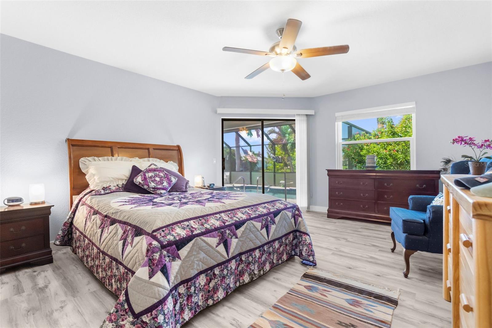 Furnished bedroom with a purple floral quilt and sliding doors overlooking a screened pool.