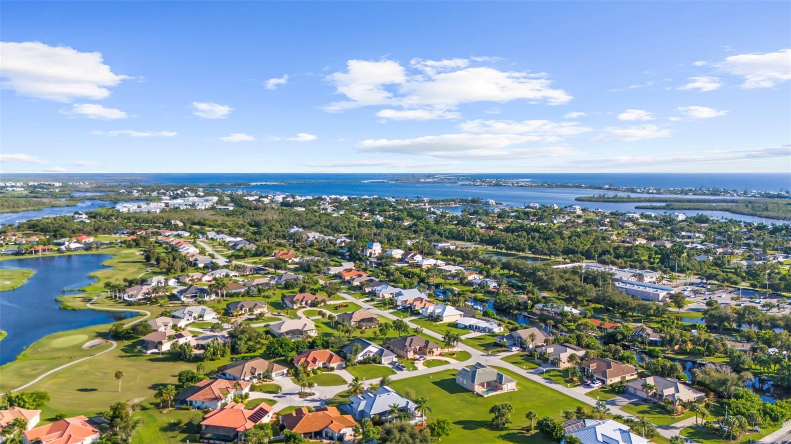 Aerial view of a coastal neighborhood with a golf course, waterways, and ocean beyond.