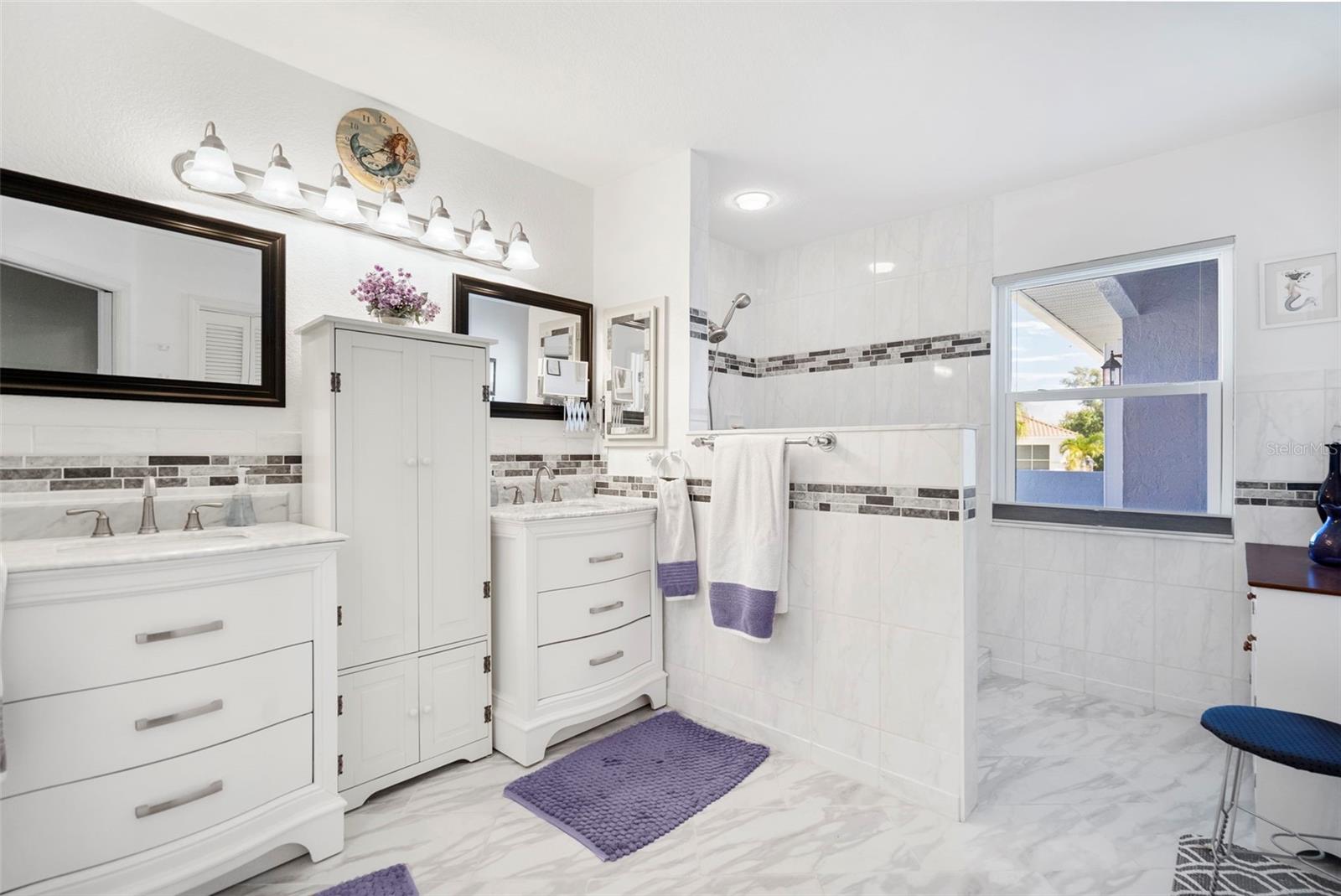 Bright bathroom with two vanity areas, marble-look tile, and a tiled shower with a dark accent stripe.