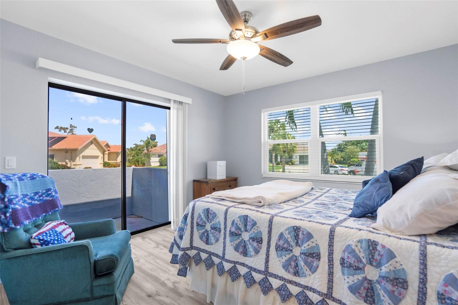 Bedroom with a patterned quilt, teal armchair, and sliding glass doors to a balcony.
