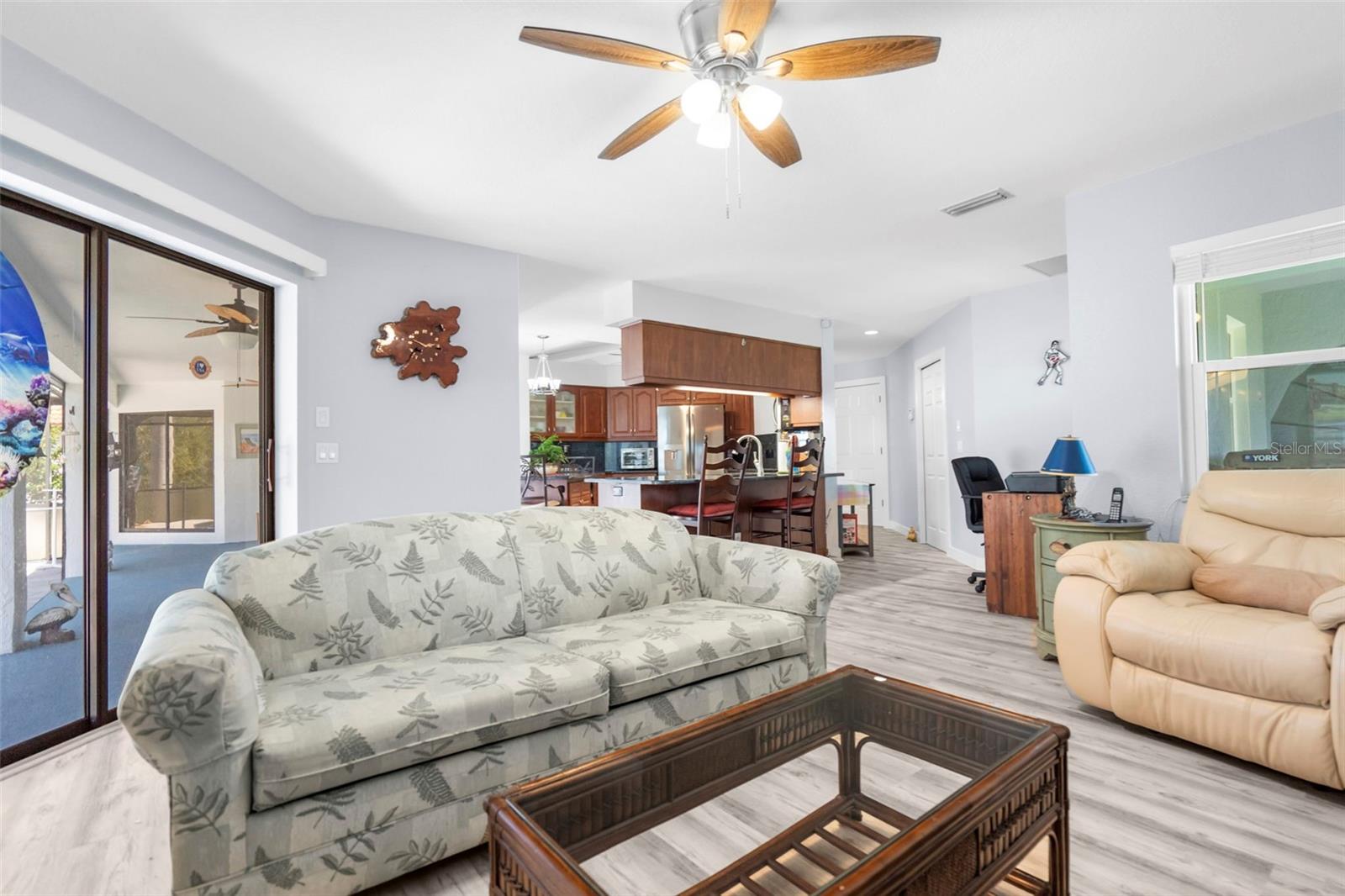 Furnished living room with a botanical-print sofa, glass-top coffee table, and open kitchen.