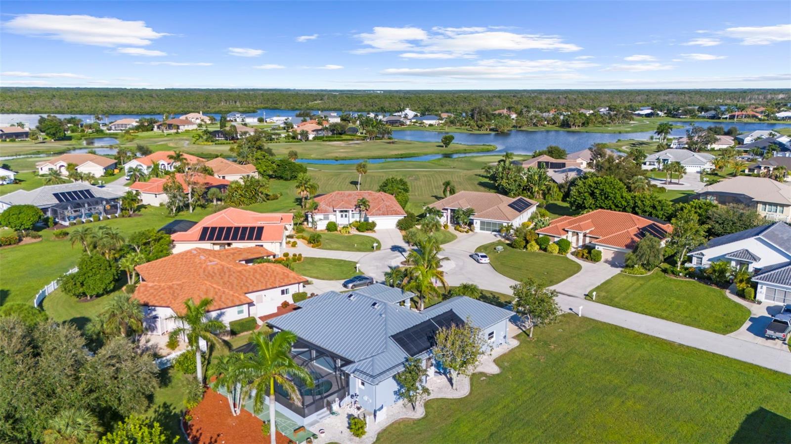 Aerial view of a home beside a lake and golf course, with a screened pool enclosure.