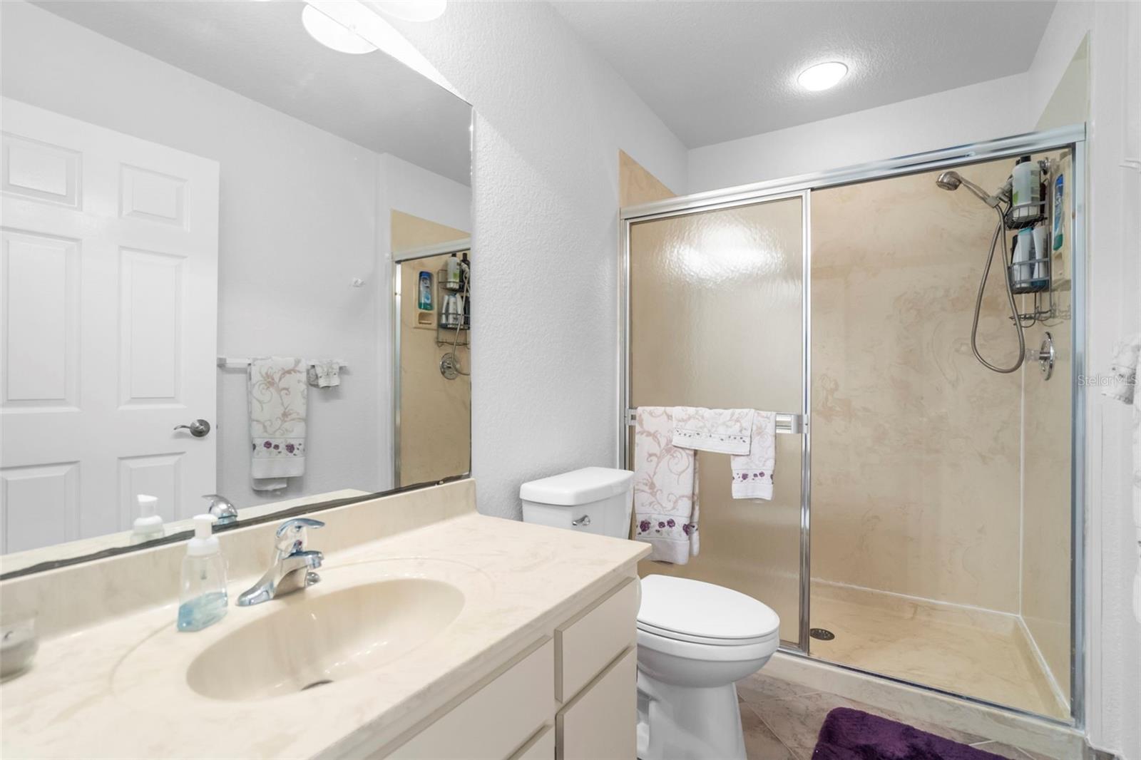 Bathroom with cream vanity, toilet, and spacious beige walk-in shower with sliding glass doors.