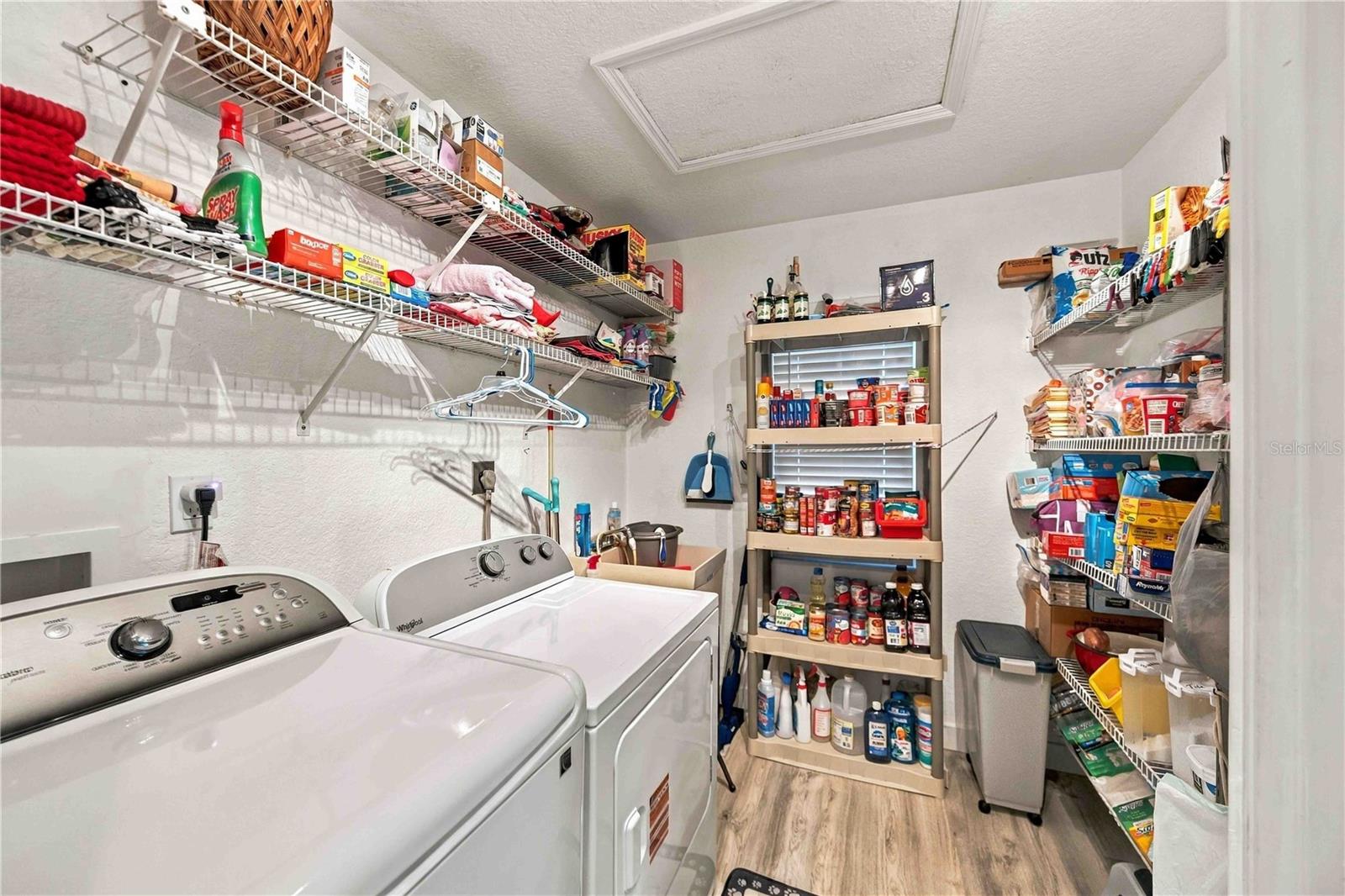 Laundry room with washer and dryer, wall shelving, and racks stocked with household supplies.