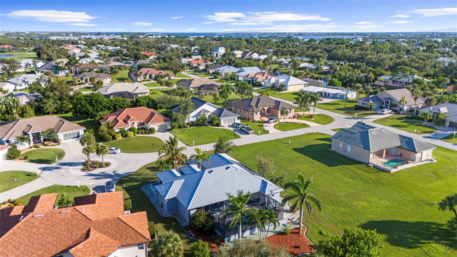 Aerial view of homes and a vacant lot, with palm trees and distant water.