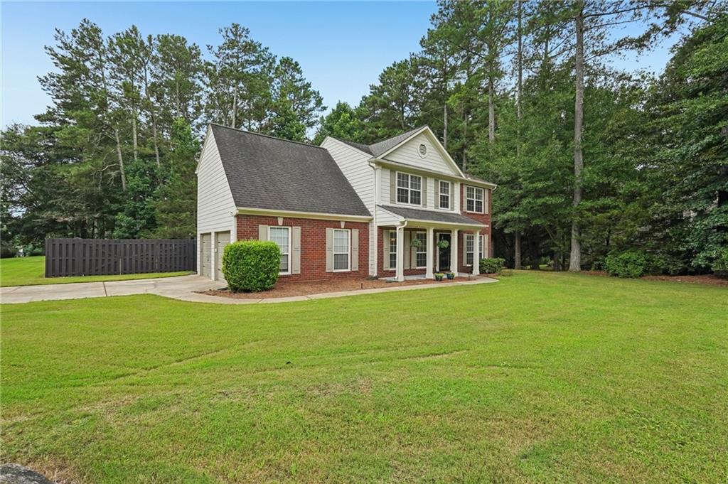 Two-story brick-and-siding home with a covered porch, broad lawn, and mature trees.