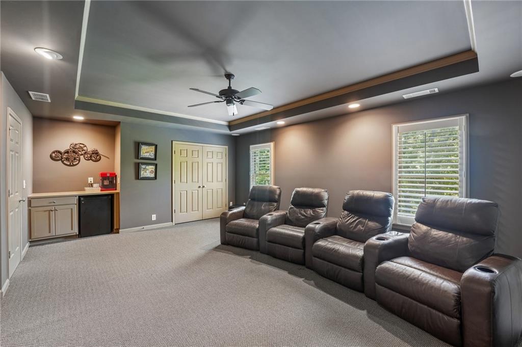Furnished home theater with dark leather recliners, gray carpet, and a tray ceiling.