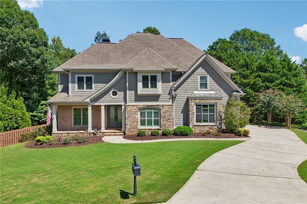 Two-story gray house with stone accents, landscaped lawn, and curved driveway.