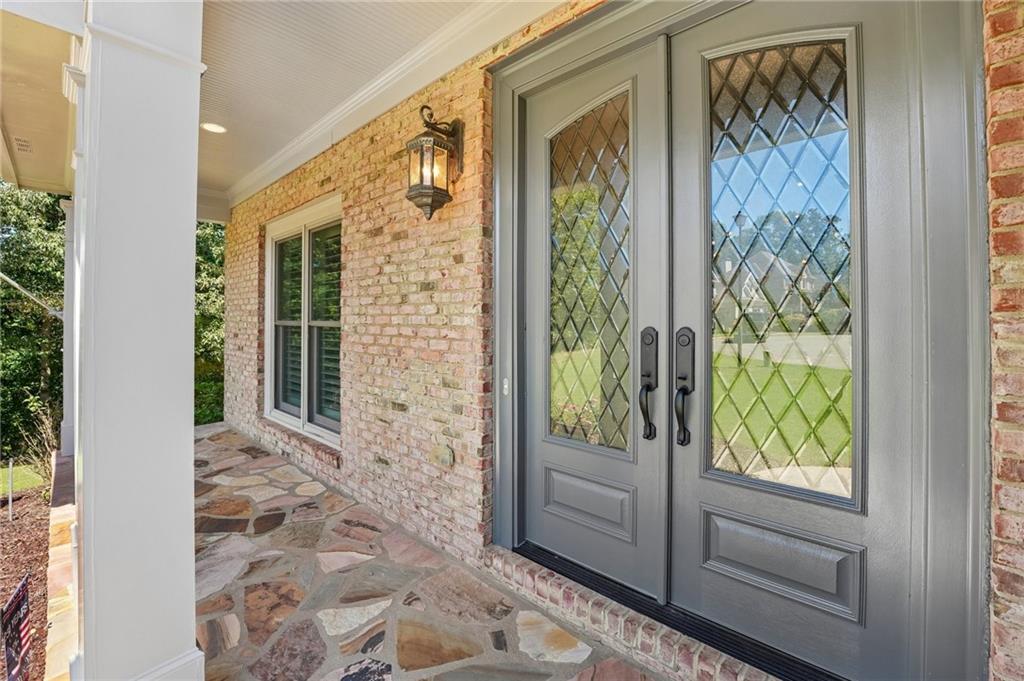 Covered front porch with diamond-glass double doors, light brick walls, and a multicolored flagstone floor.